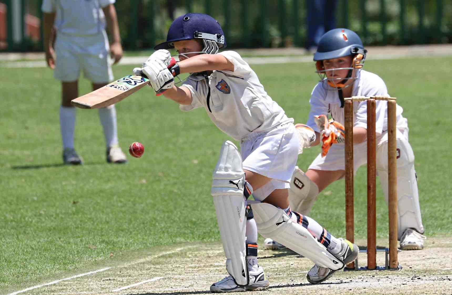 Young cricket batter playing a defensive shot as wicketkeeper waits